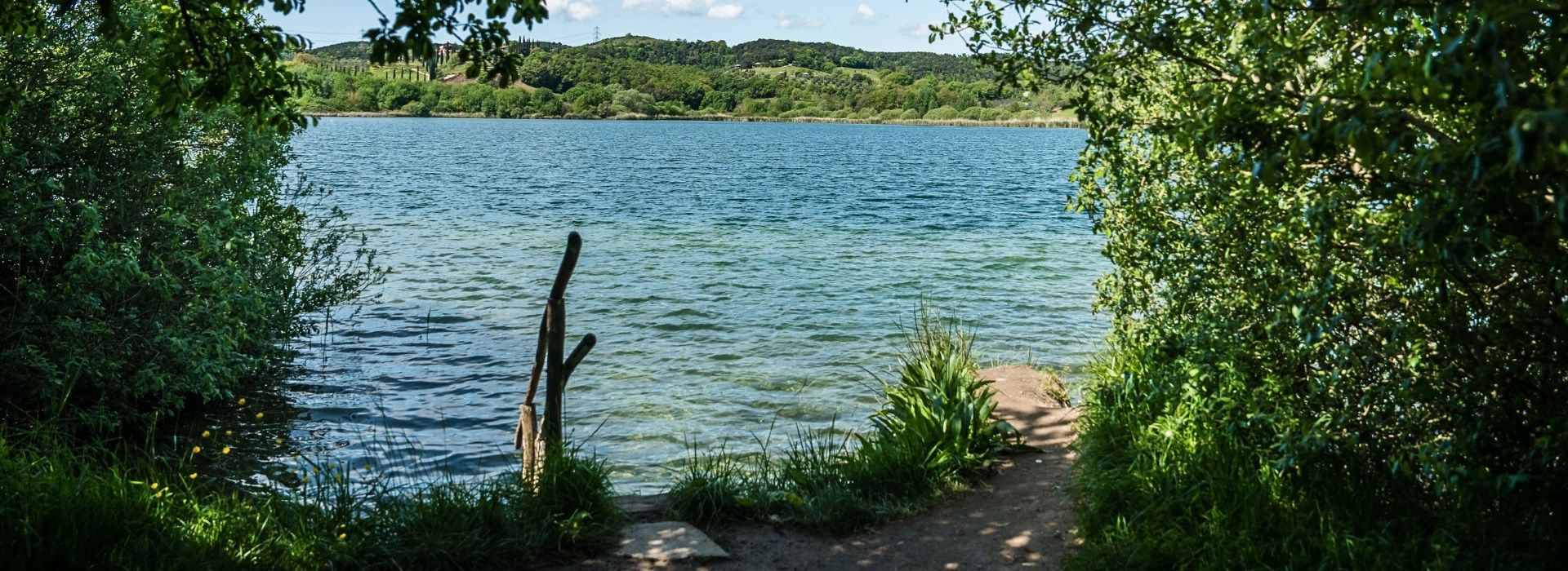 A glimpse of the clear, blue waters of Lago dell'Accesa seen through the vegetation on the shore, with the wooded hills of Maremma in the background