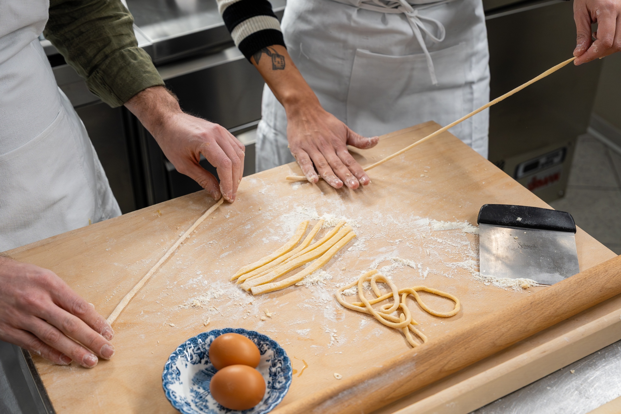 Hands shaping pasta on a floured wooden board during a Tuscan cooking class