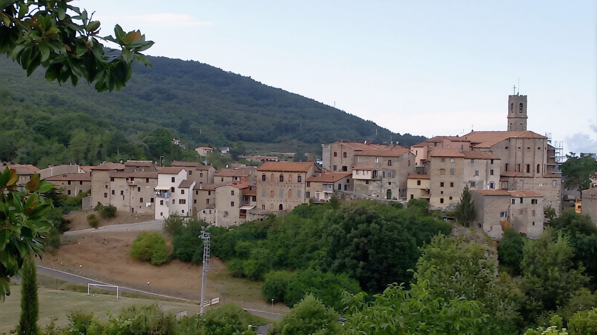 Veduta panoramica del borgo medievale di Castelnuovo di Val di Cecina con le case in pietra dai tetti in cotto, il campanile della chiesa e le colline boscose sullo sfondo