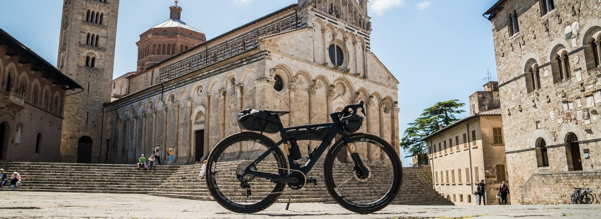 Bicicletta con borse da bikepacking parcheggiata in Piazza Duomo a Massa Marittima, con la facciata romanica della Cattedrale di San Cerbone sullo sfondo, tappa del Grande Tour della Maremma in bici
