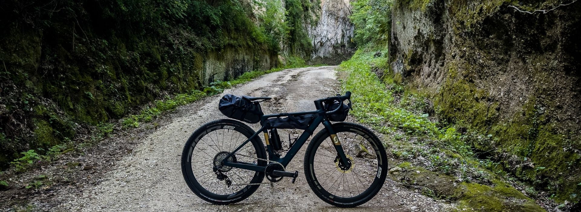 Bicicletta con borse da bikepacking su un sentiero sterrato tra pareti rocciose di tufo, tipiche delle Vie Cave etrusche vicino Pitigliano e Sorano, tappa del Grande Tour della Maremma - Anello Sud