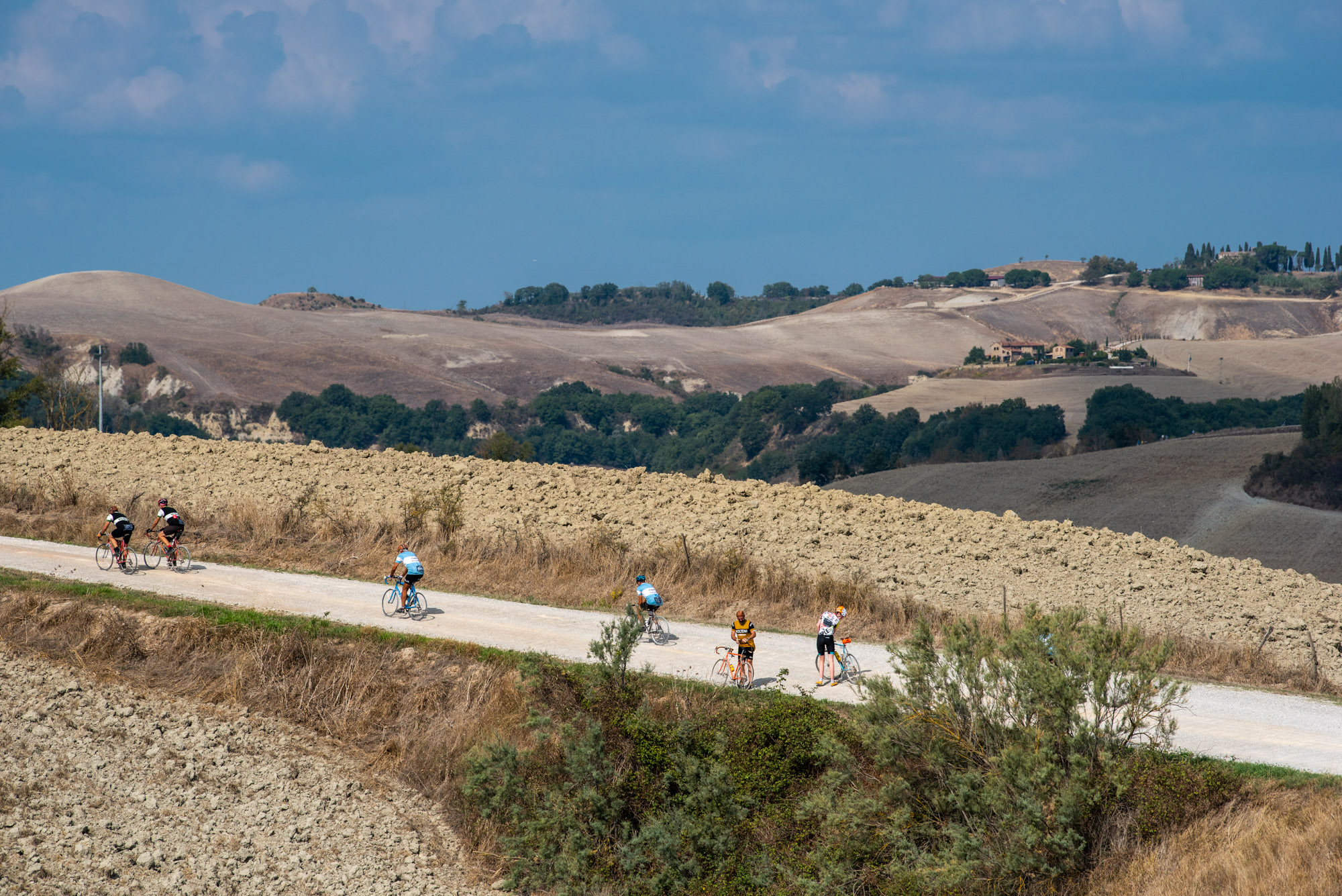 Gruppo di ciclisti su biciclette d'epoca che pedalano su una tipica strada bianca sterrata
