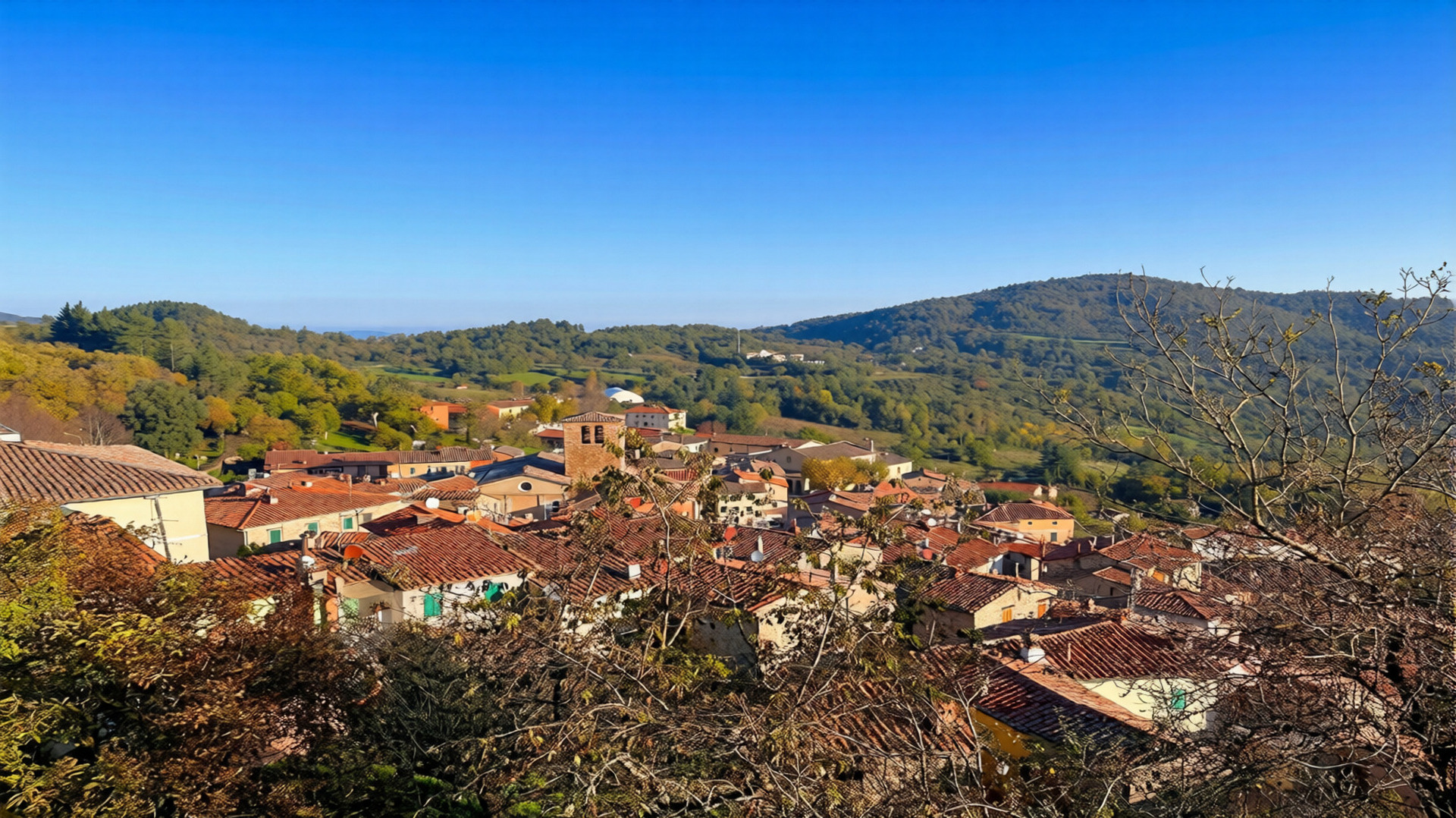 Vista panoramica dall’alto del borgo di Montieri con i tetti in cotto delle case e le colline verdi della Maremma collinare sullo sfondo sotto un cielo azzurro limpido in autunno