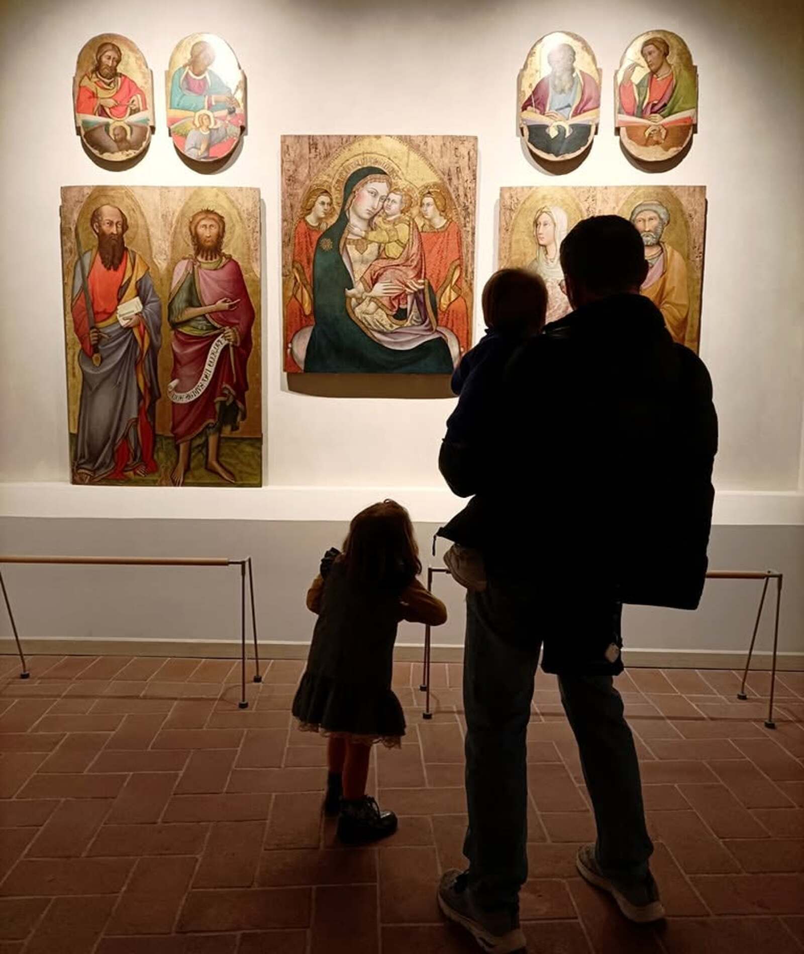 Una delle sale del museo con un adulto e due bambini di spalle che osservano i dipinti