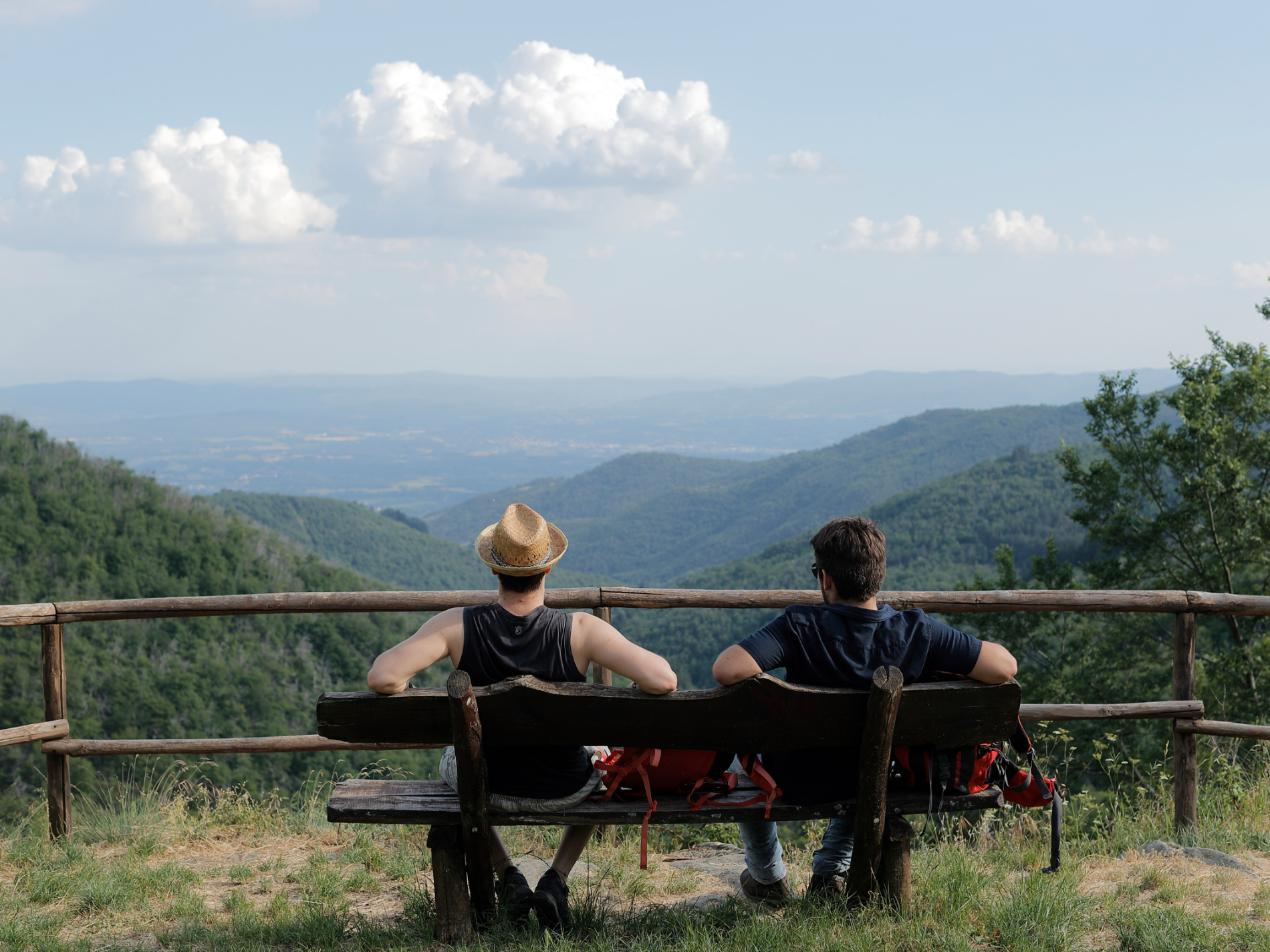 Escursionisti in sosta su una panchina con vista su una vallata circondata da montagne e foreste.