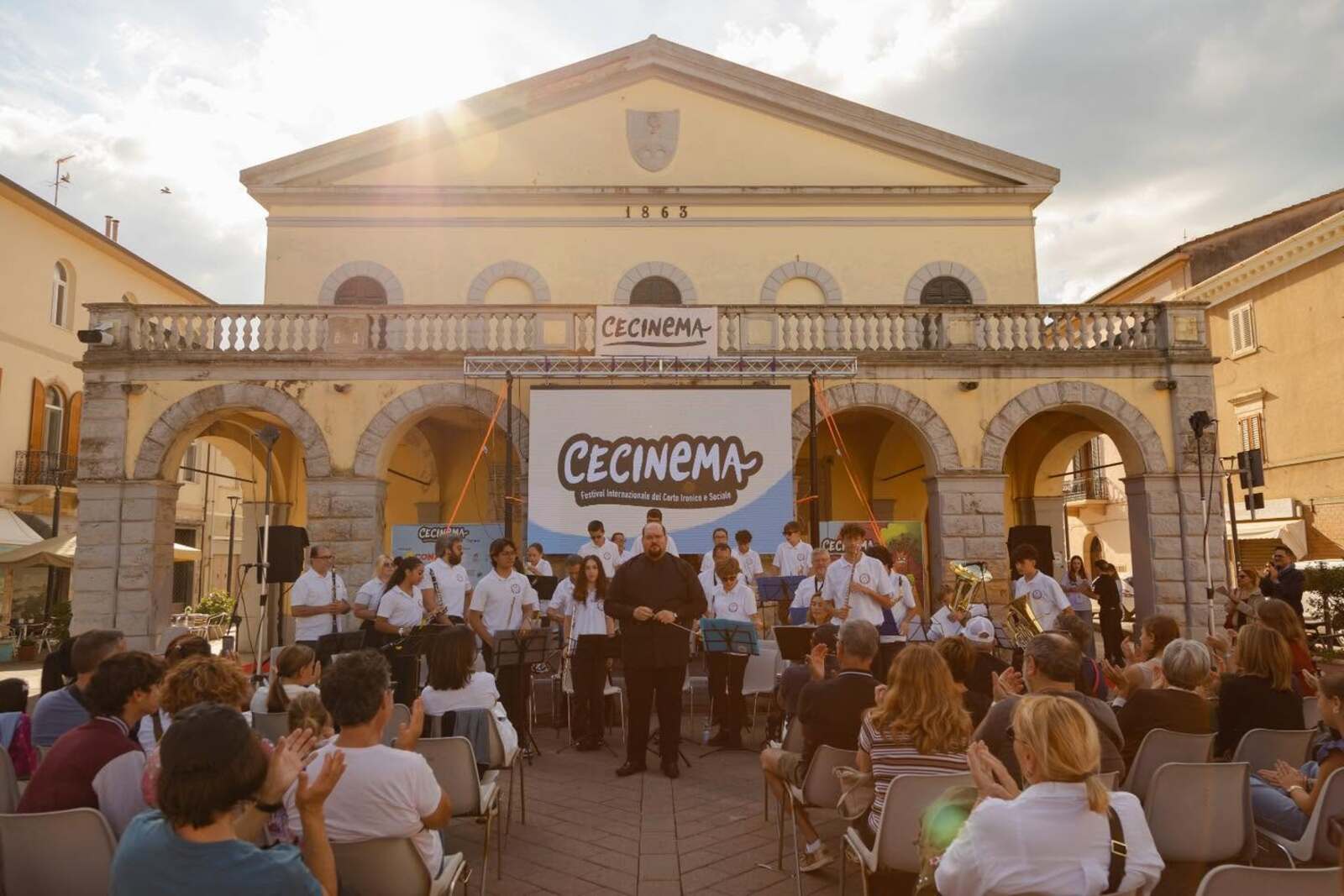 Concerto all’aperto davanti al Palazzetto dei Congressi di Cecina durante Cecinema, con musicisti sul palco e pubblico seduto in piazza.