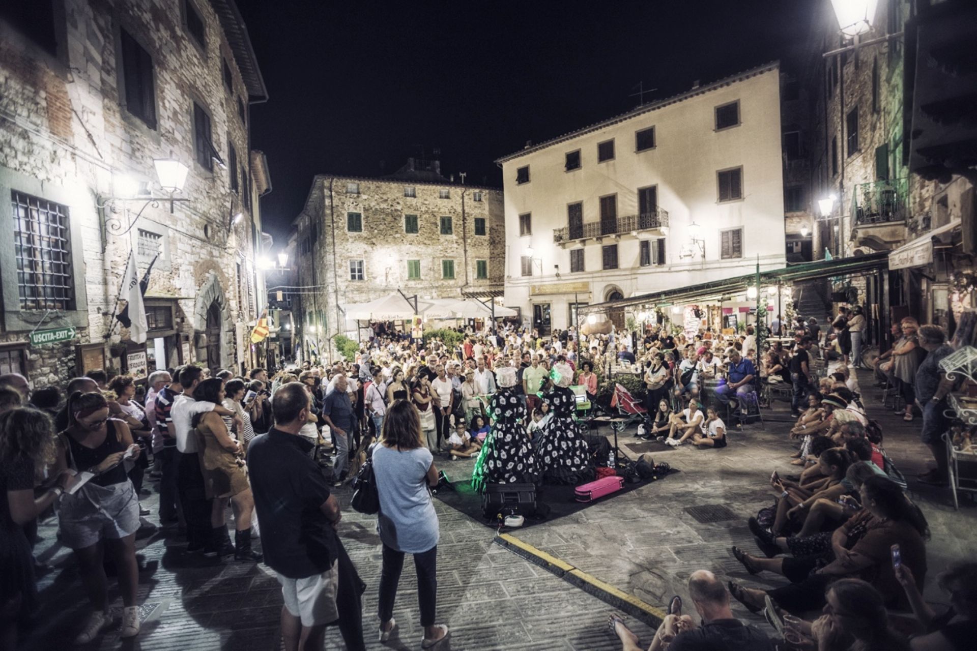 Persone che seguono uno spattacolo nella piazza piena di gente ed illuminata