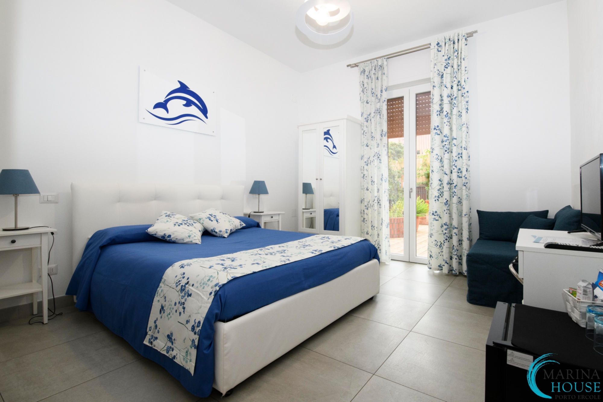 Una stanza da letto del bed and breakfast Marina House Porto Ercole con biancheria bianca e blu e arredi in tinta