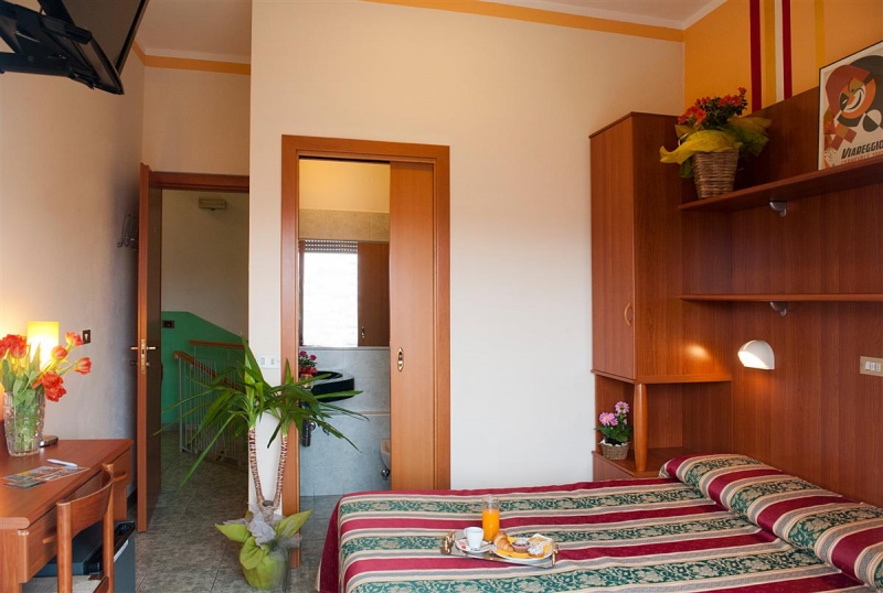 Una camera matrimoniale da cui si vede la porta del bagno aperta e la scrivania con sedia tutto in legno