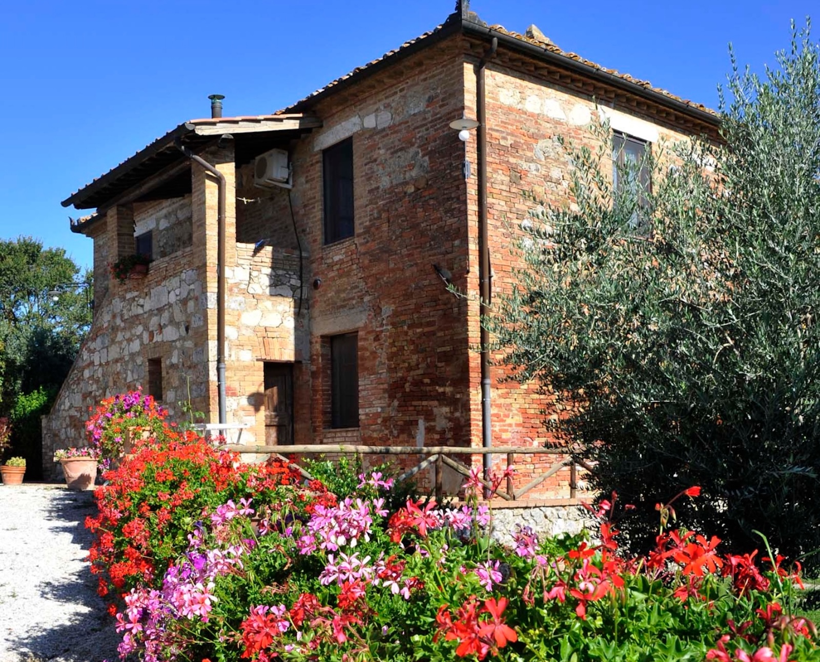 Facciata in pietra e mattoni del Podere il Moro con fiori colorati in primo piano e ulivo in Toscana