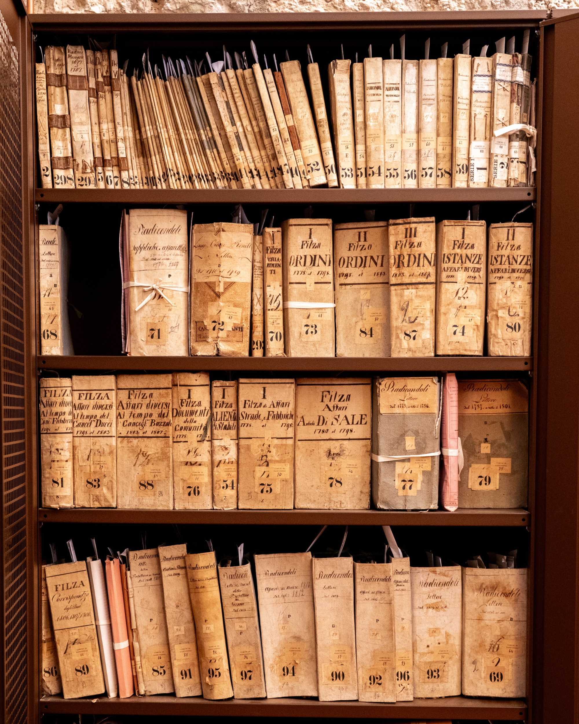 A shelf in the Historical Archive of the Municipality of Radicondoli containing old ledgers, files and paper documents, organized and preserved in vintage binders.