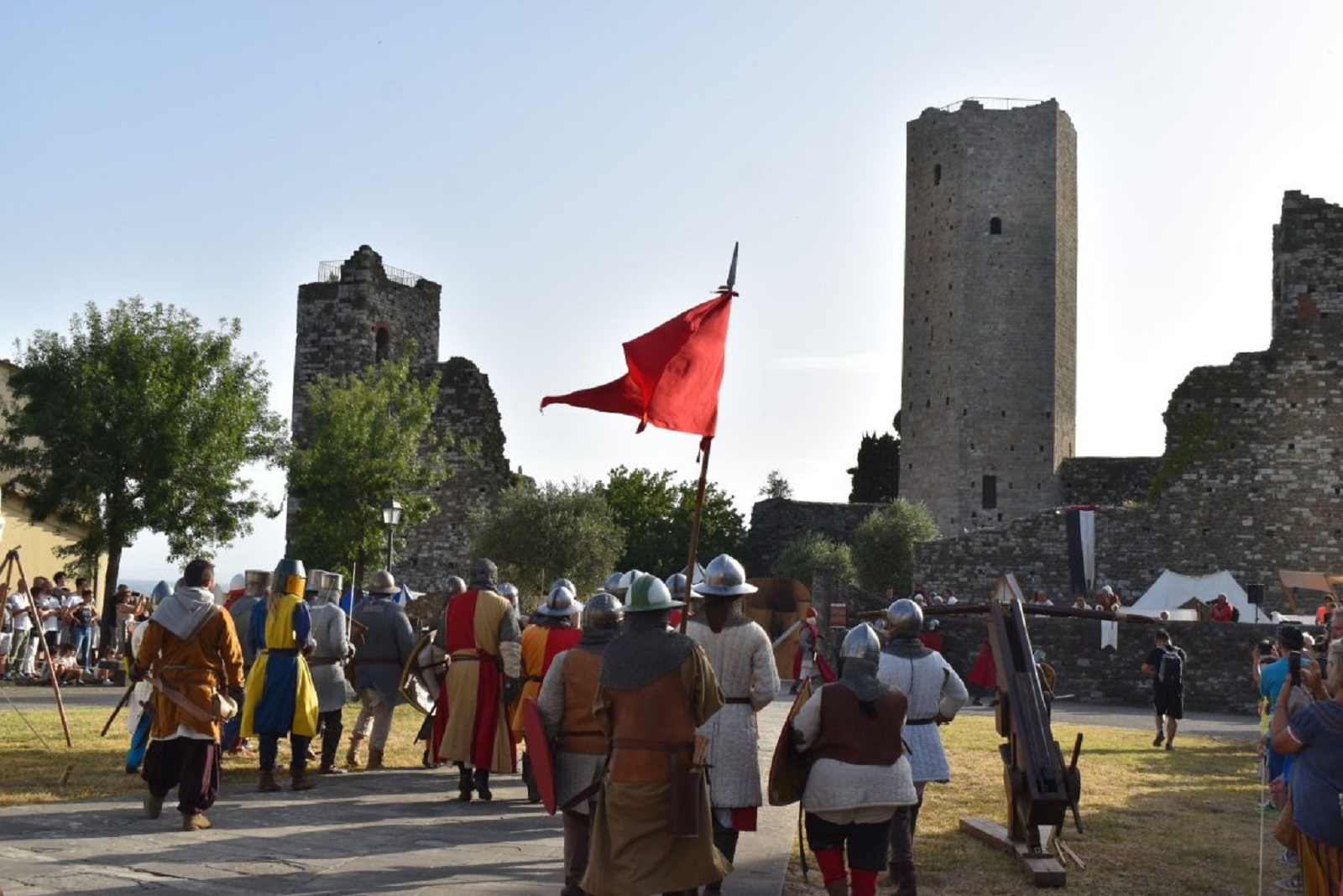 Statisten in Rüstung und Kostümen ziehen mit einer roten Fahne vor der Rocca di Castrucci vorbei
