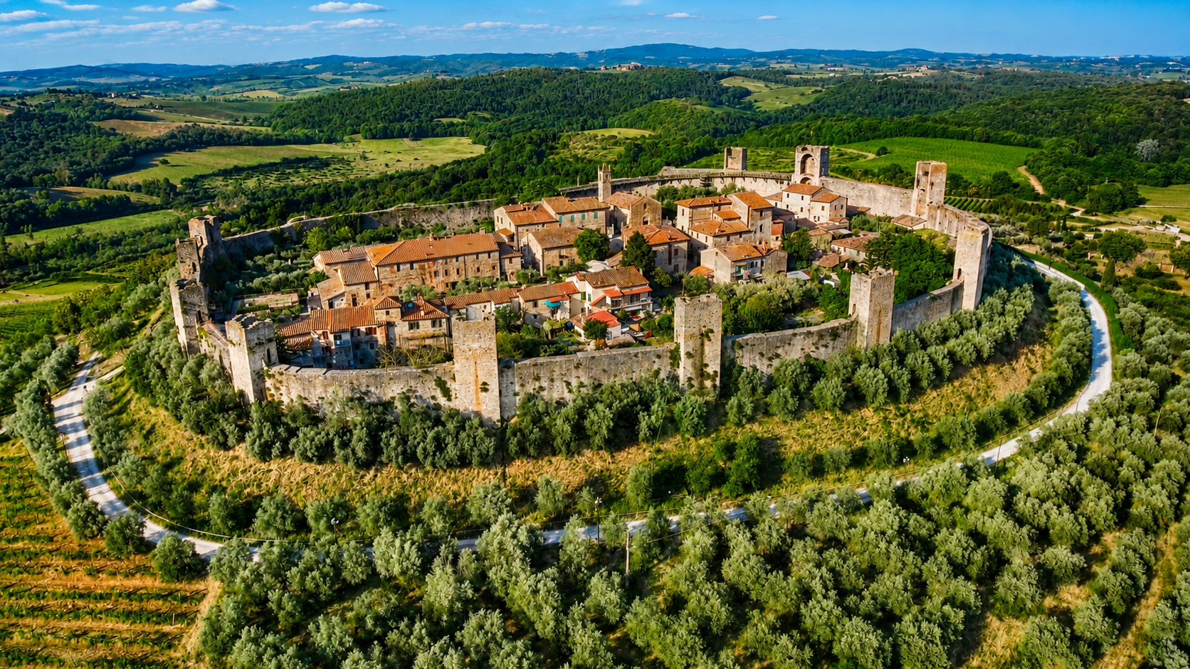 Vista aerea del borgo medievale di Monteriggioni con le sue mura circolari e le torri intatte, circondato da oliveti, vigneti e colline toscane verdi