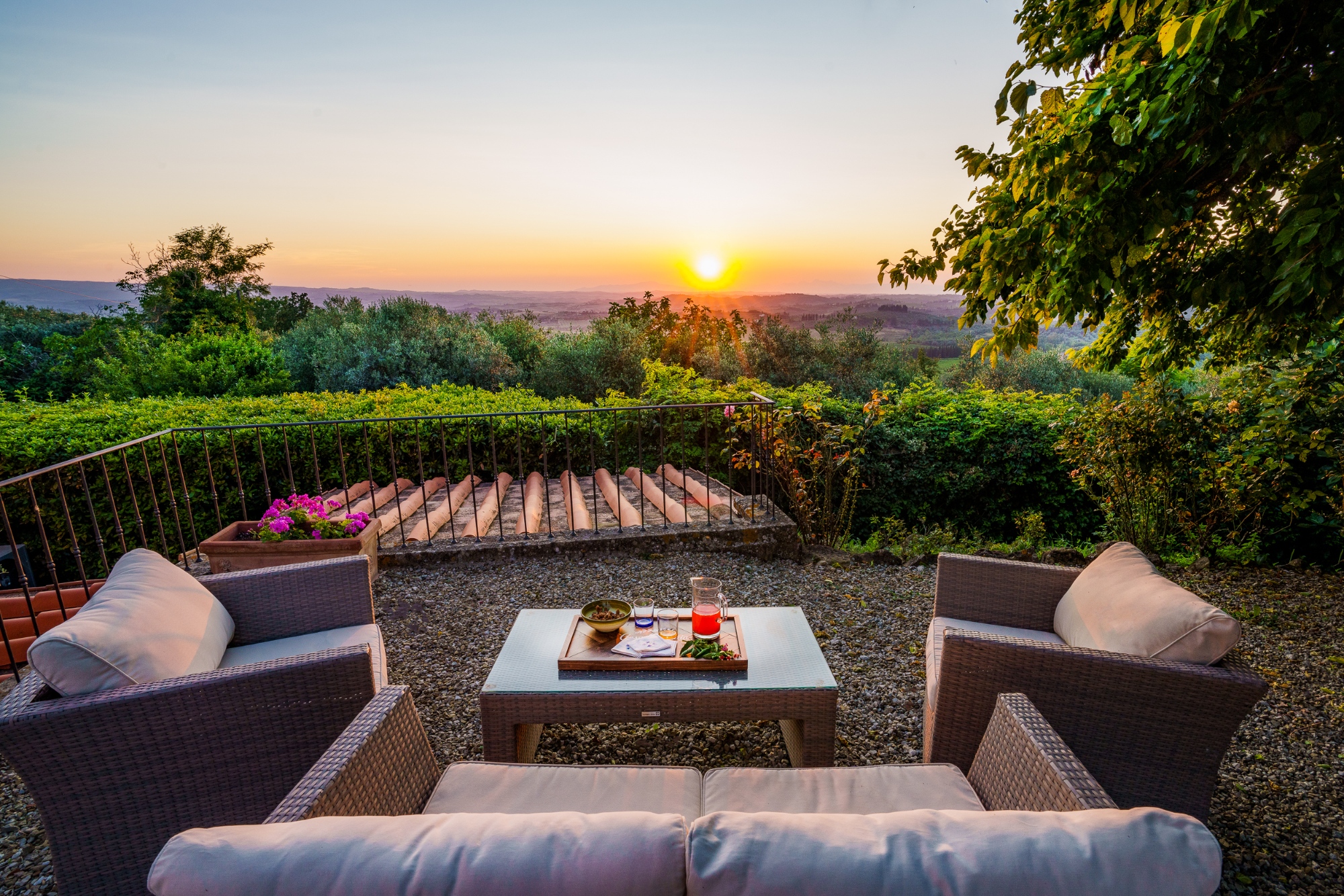 Terrazza esterna di Casa Pietraia a Certaldo con divani in rattan e tavolino con bevande, affacciata sulle colline toscane al tramonto