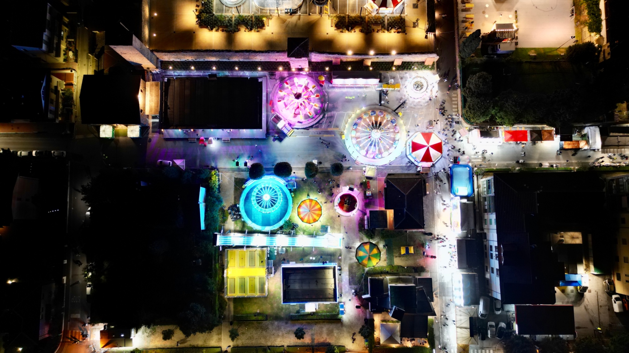 Vista aerea notturna della fiera di Terranuova Bracciolini, con una grande ruota panoramica illuminata e lo storico centro città sullo sfondo.