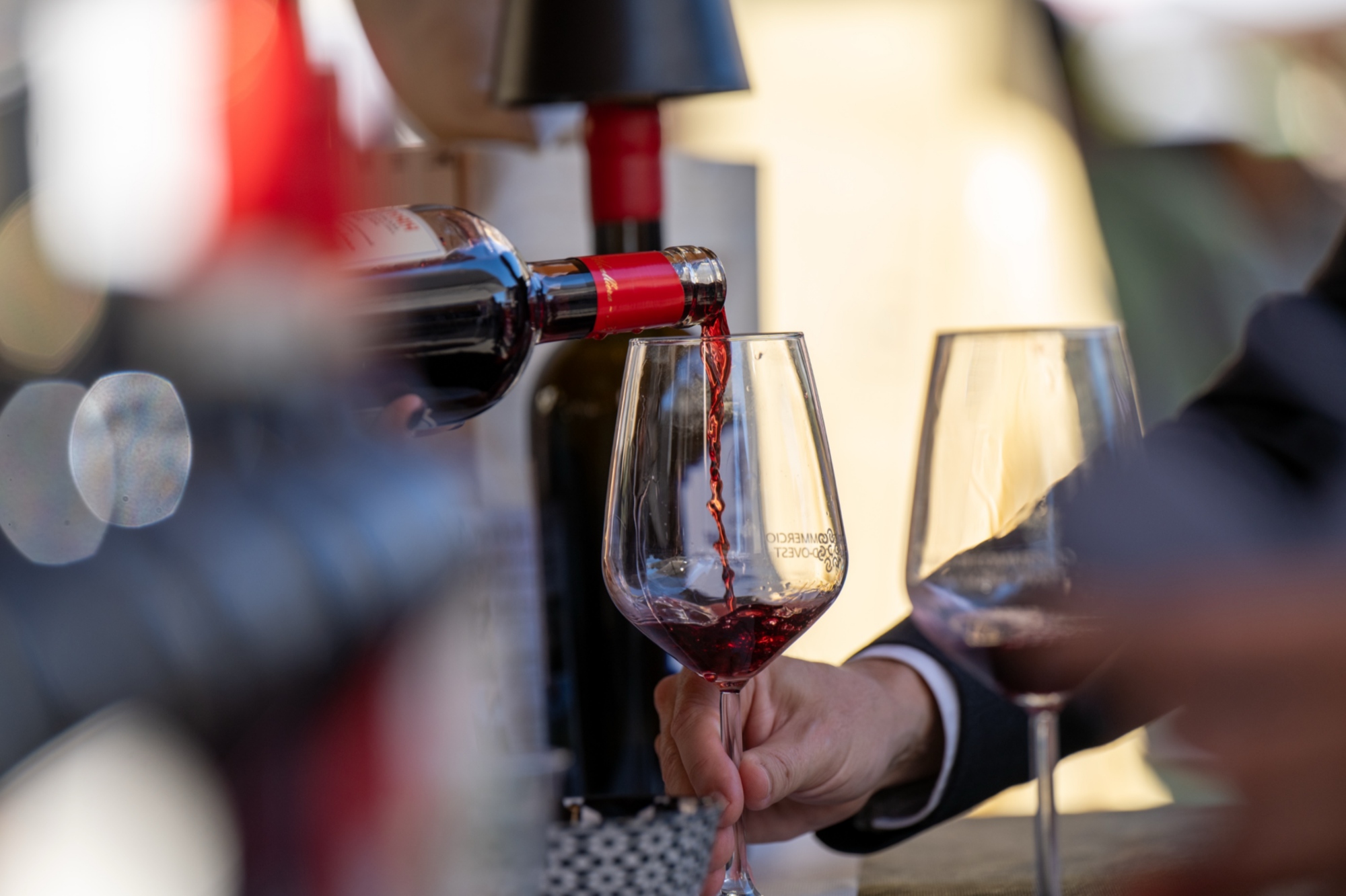Vino rosso versato da una bottiglia in un calice sorretto da una persona durante una degustazione.