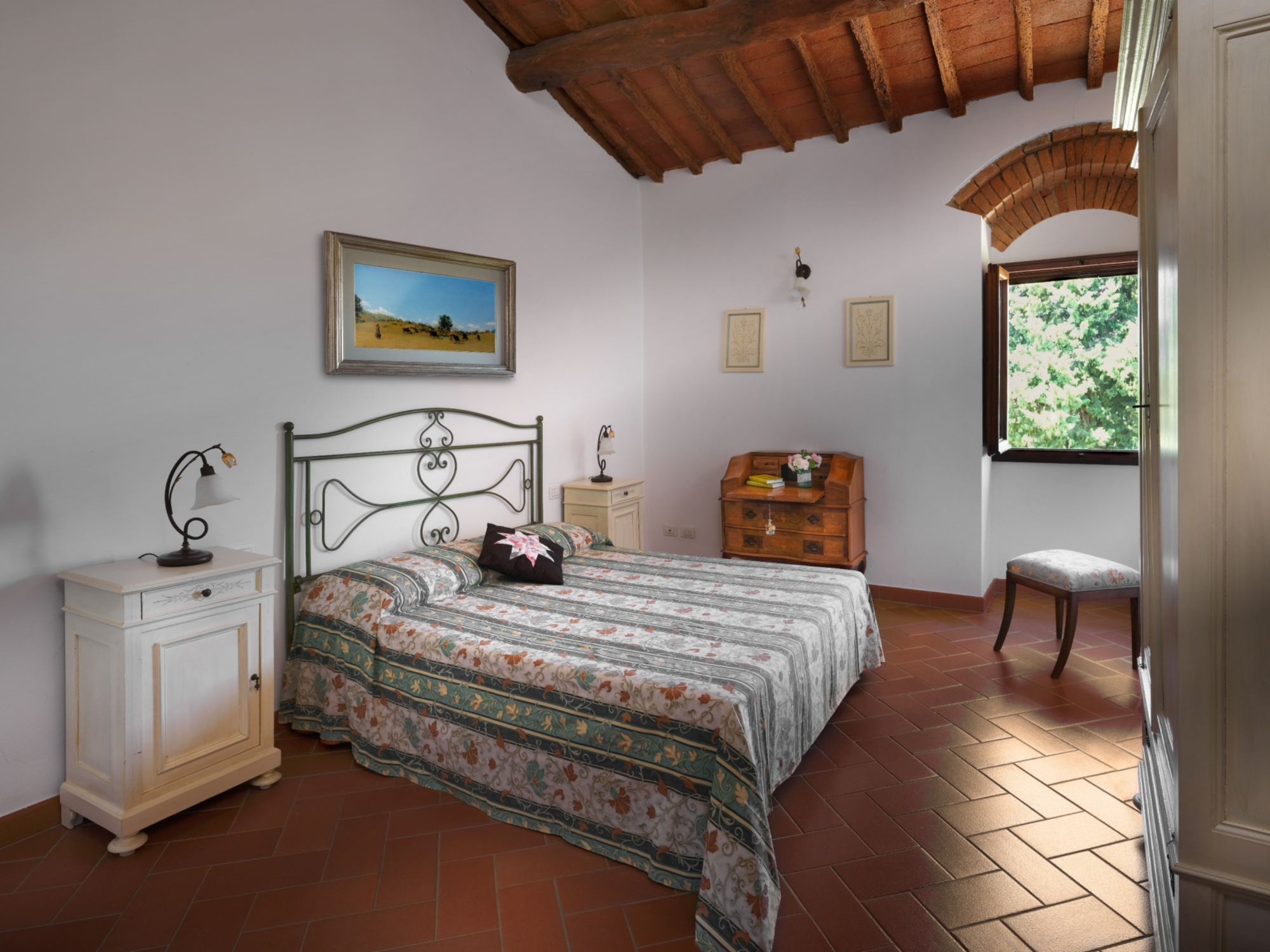 Una camera matrimoniale con letto in ferro, soffitto con travi a vista e il classico mobilio in legno 