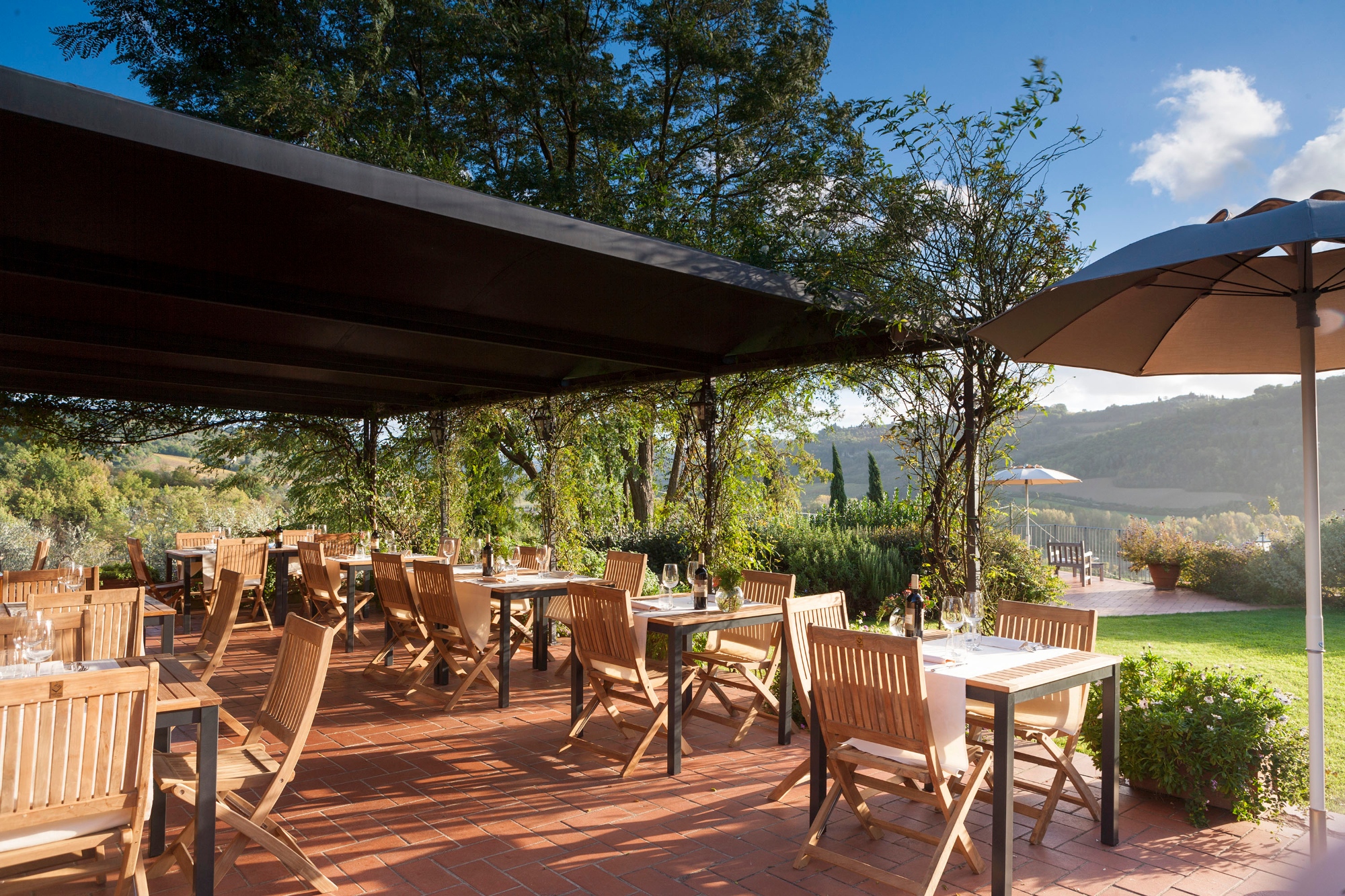 The outdoor space of the Relais Poggio Borgoni with wooden tables and chairs