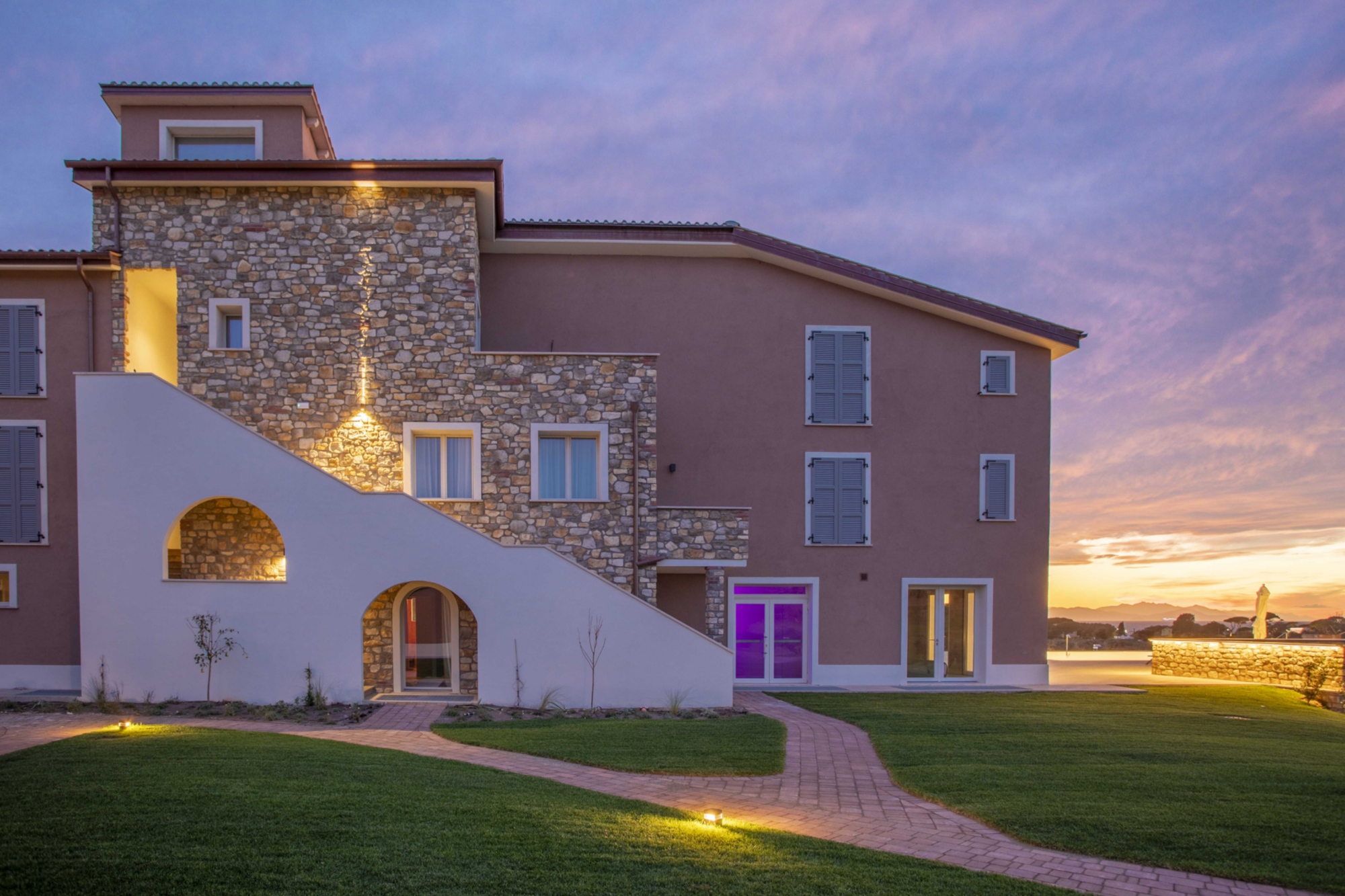 Un viale piastrellato con l'entrata di Riva Toscana Golf Resort & SPA con una luce viola