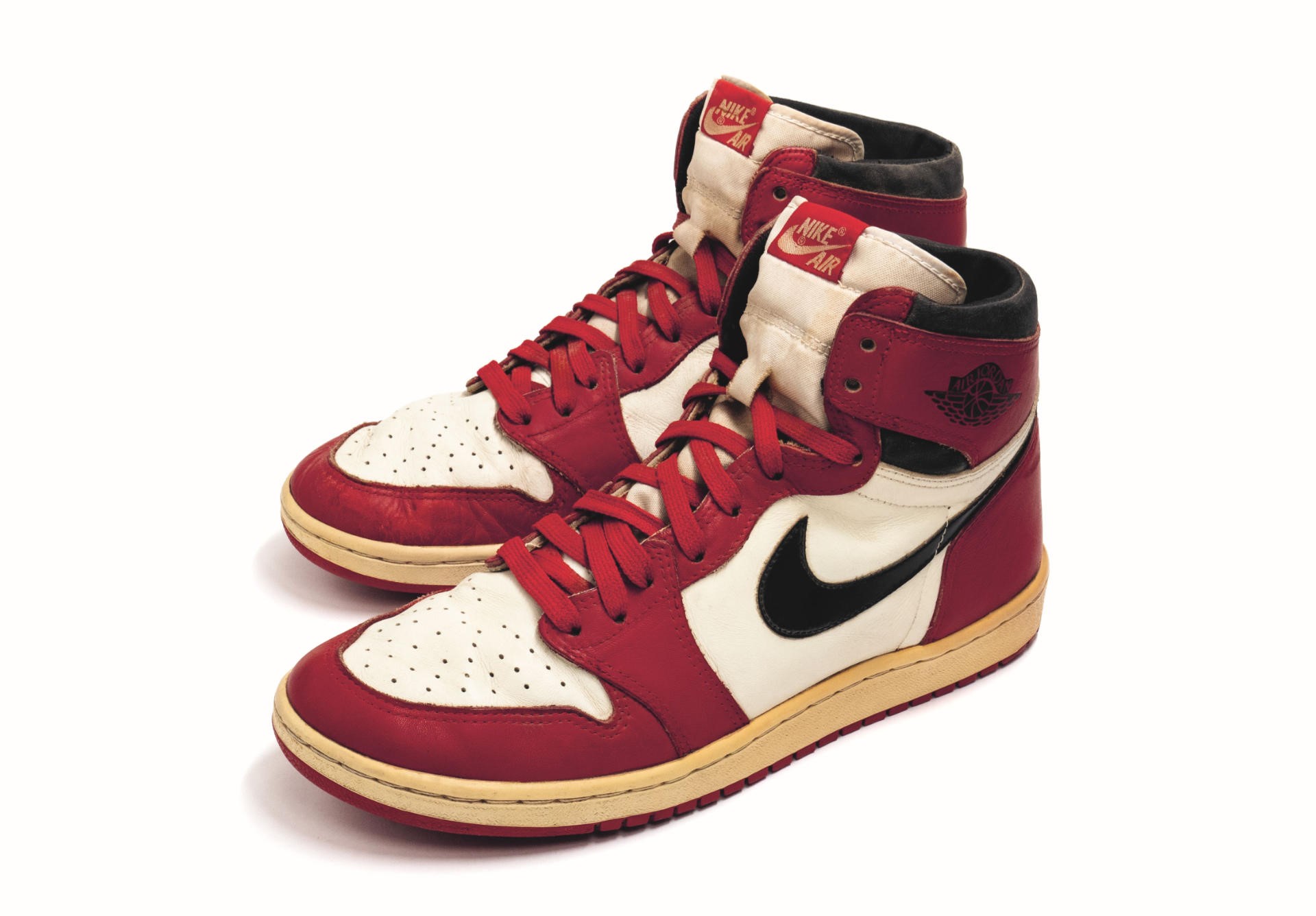 Paio di sneakers Nike Air Jordan alte, rosse, bianche e nere, con lacci rossi e suola color crema, su sfondo bianco.