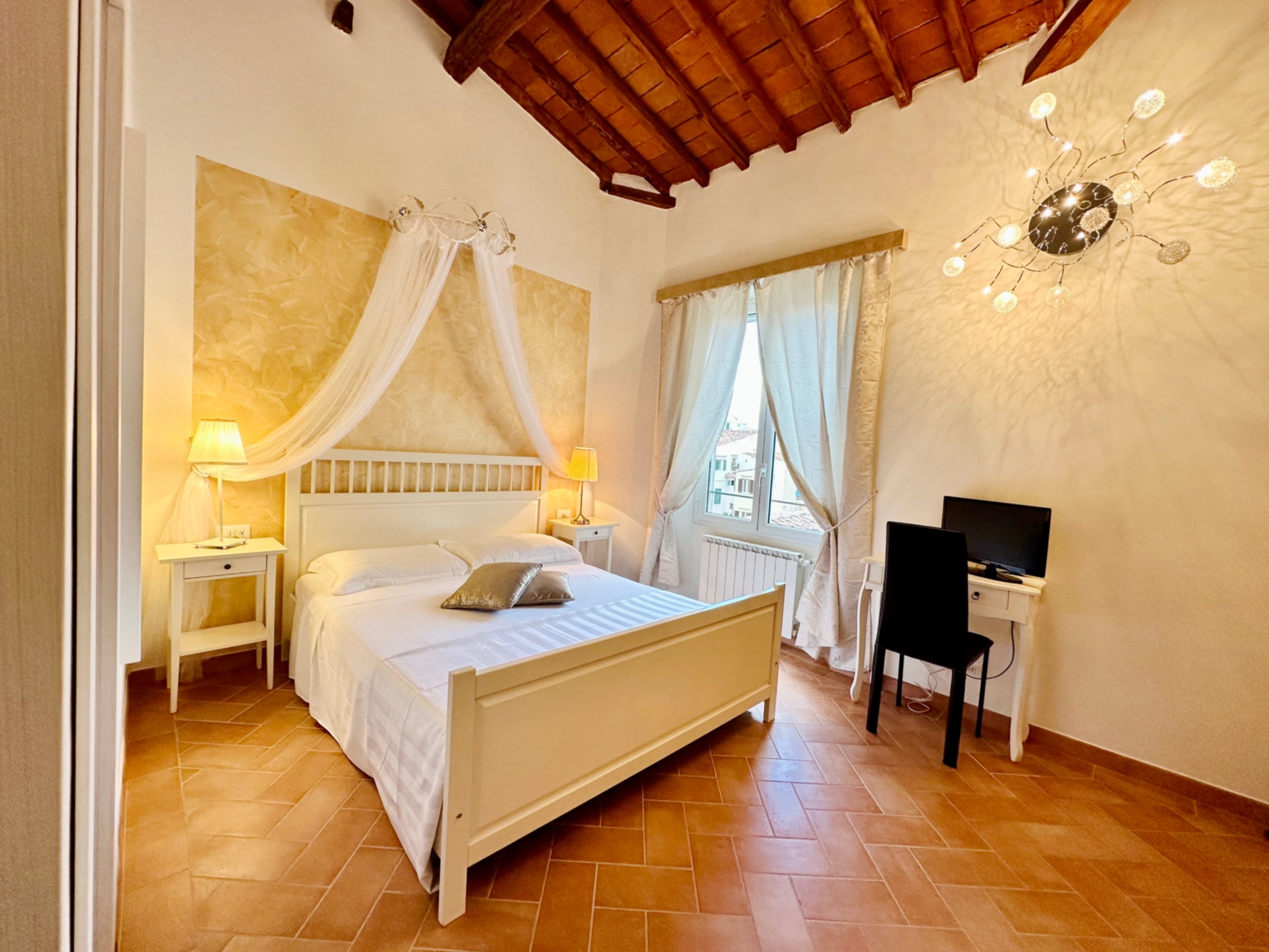 Room with a four-poster double bed, terracotta flooring, exposed beams and views over the rooftops of Florence