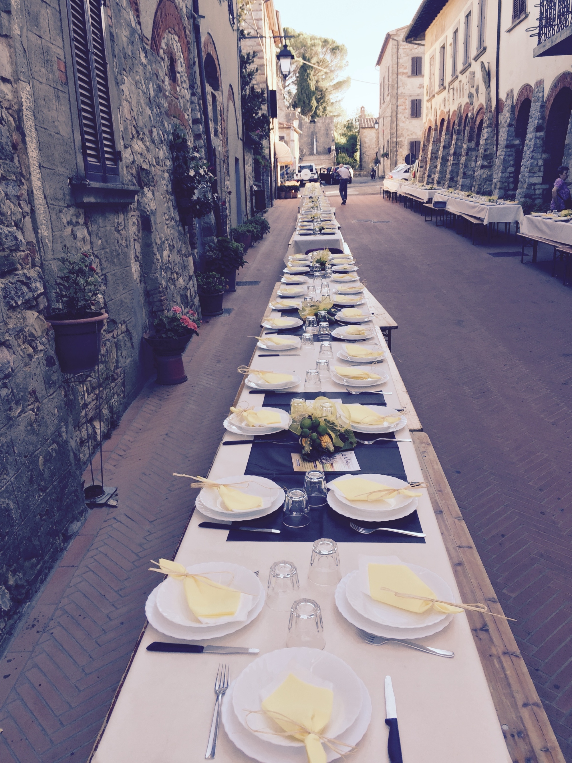 Allestimento della cena fine estate nella via principale del borgo, con tavoli apperecchiati e curati