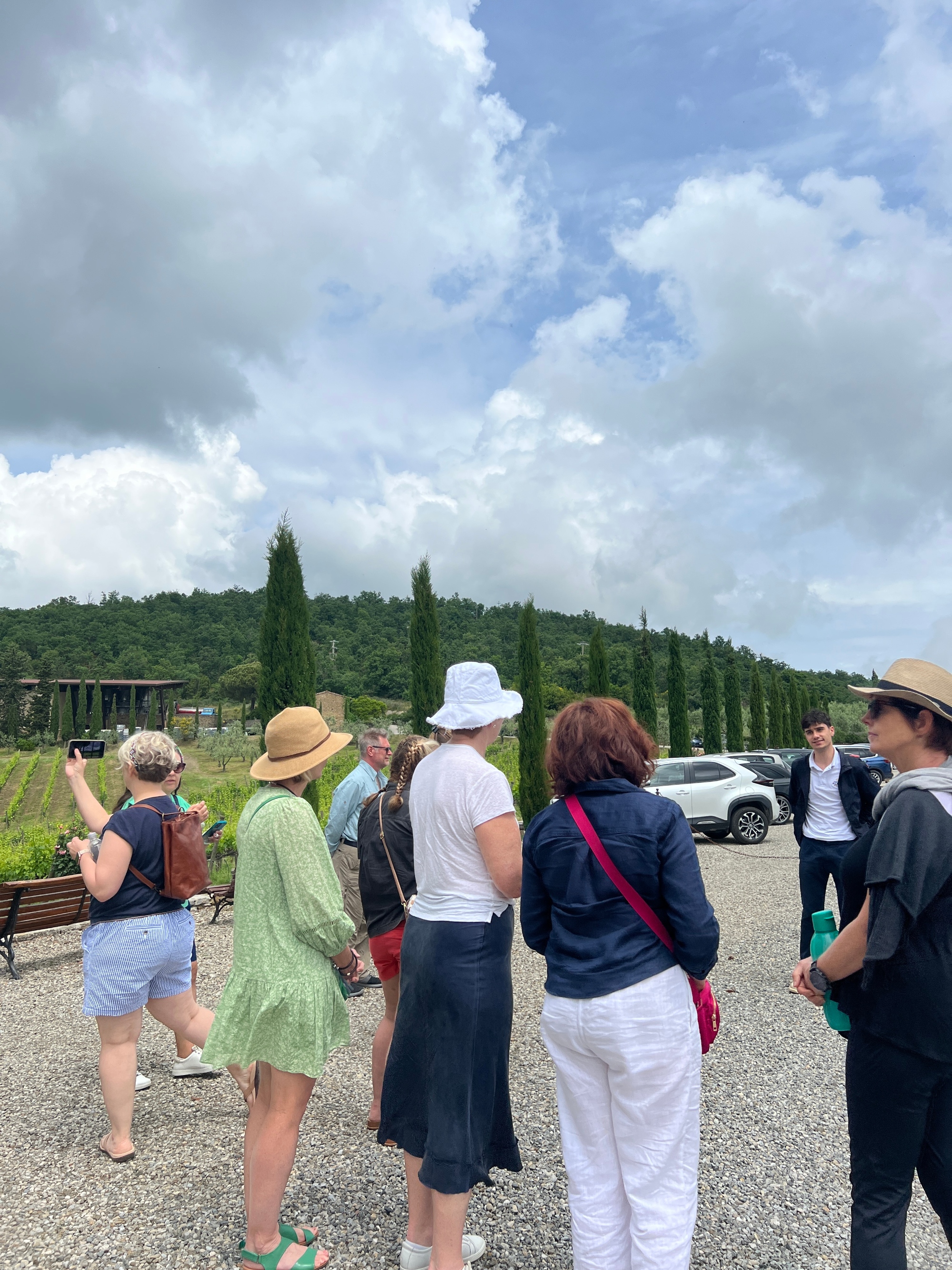 Un gruppo di visitatori ascolta una guida locale in una storica cantina immersa tra le colline del Chianti, circondati da vigneti e botti di rovere.