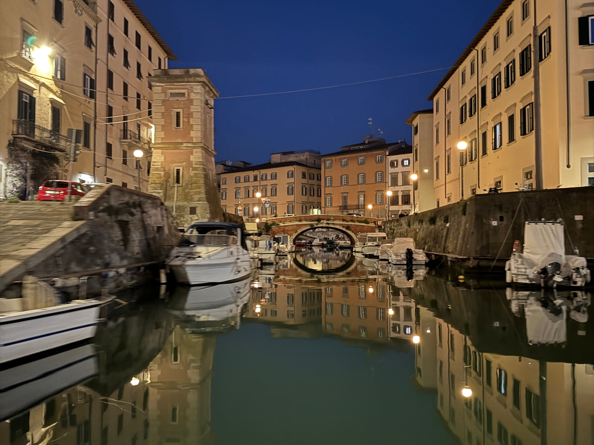 Canale mediceo di Livorno di notte con barche ormeggiate, ponte ad arco in mattoni illuminato e palazzi storici che si riflettono nell'acqua ferma
