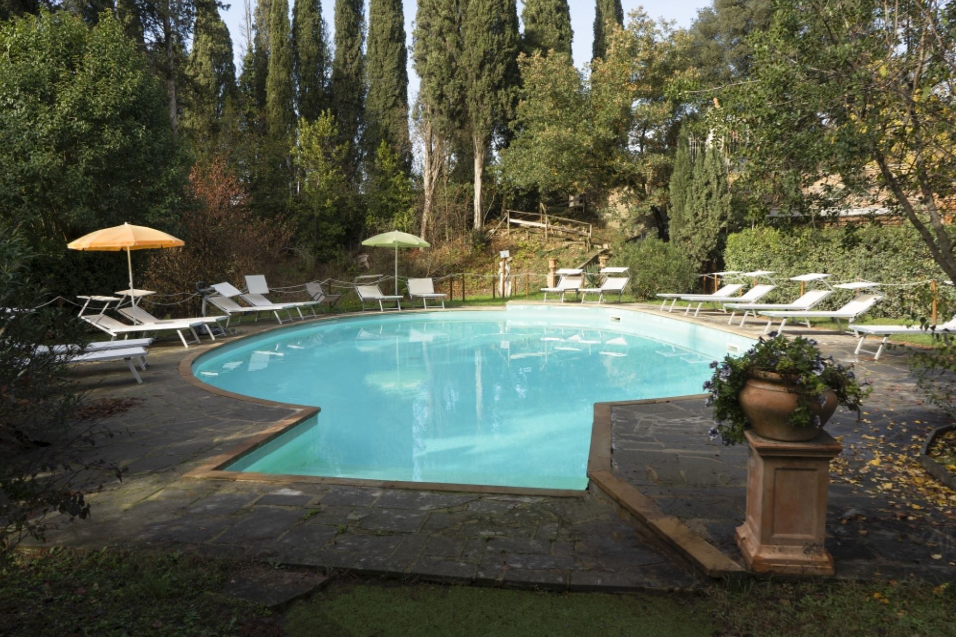 La piscina di Borgo Dolciano con sdraio e ombrelloni circondata da alberi e prato verde 