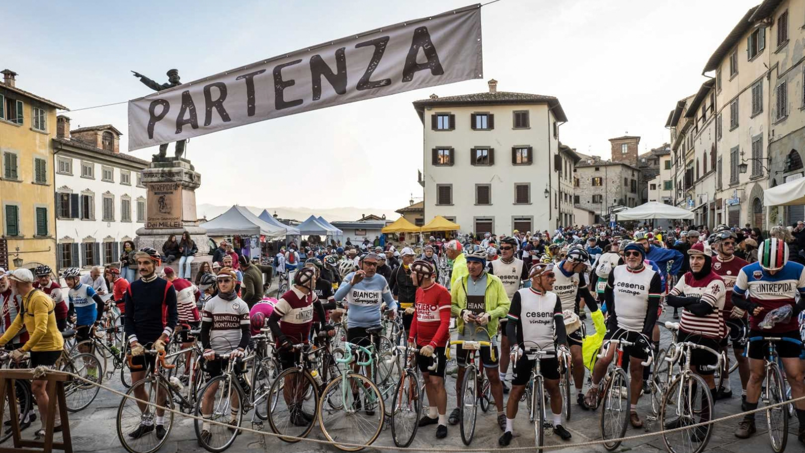 Ciclisti con abbigliamento e biciclette d’epoca radunati sotto lo striscione di partenza de L’Intrepida ad Anghiari