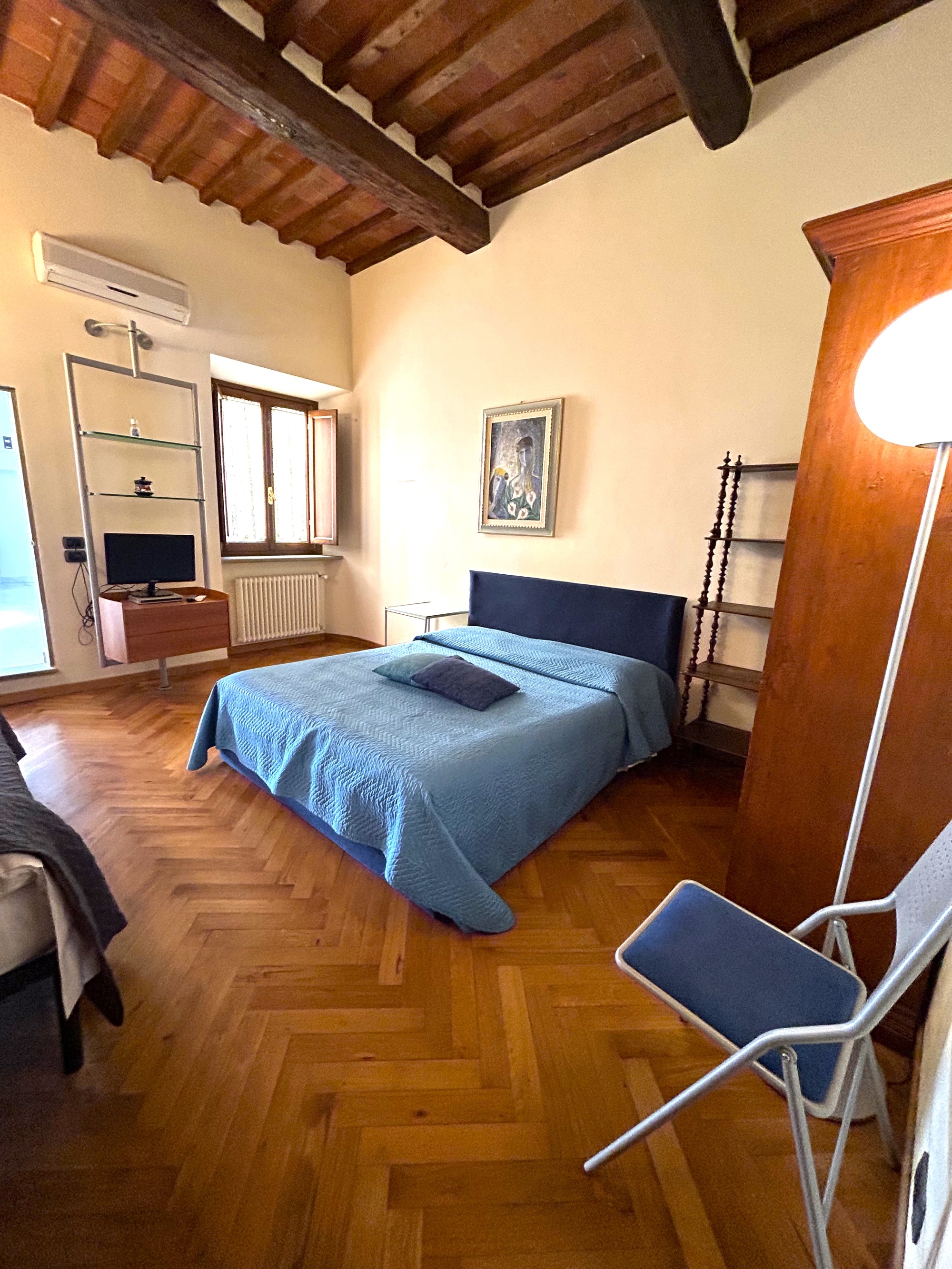 Camera matrimoniale con parquet a lisca, travi a vista e arredo di colore blu
