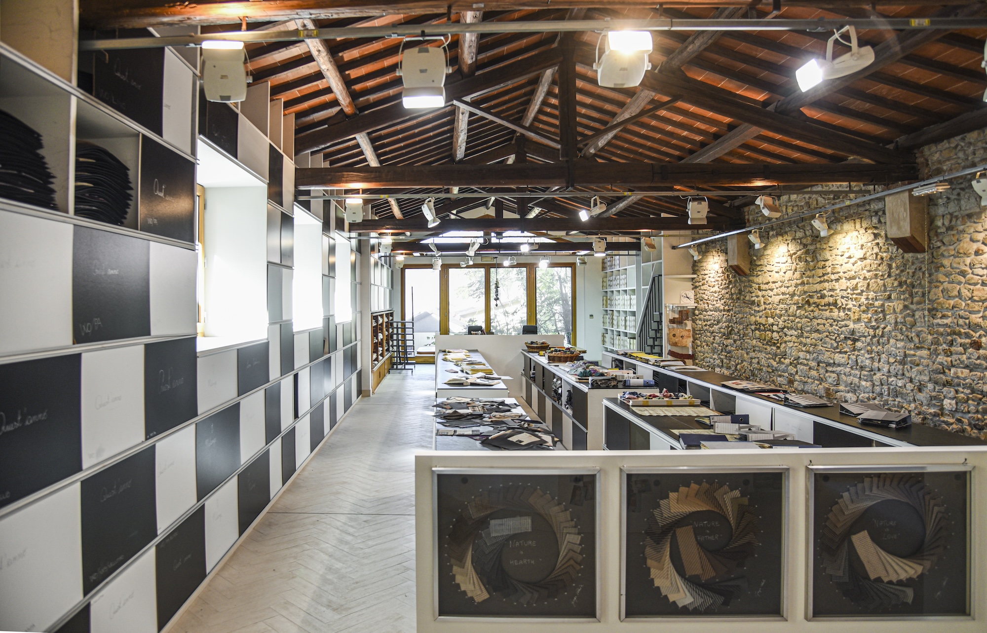 Intérieur du showroom de la filature Lanificio Lucchesi : au centre de la pièce, de longues tables blanches présentent de manière ordonnée divers échantillons et morceaux de tissu