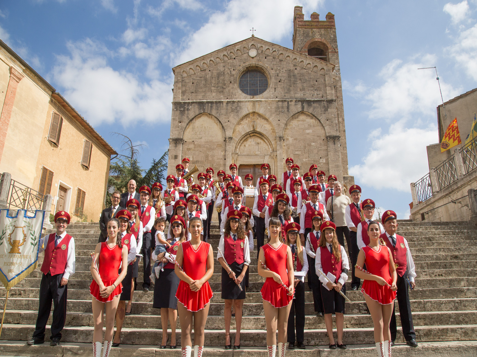 Filarmonica in posa sui gradini della Basilica di Sant’Agata ad Asciano, con musicisti in divisa e strumenti musicali.