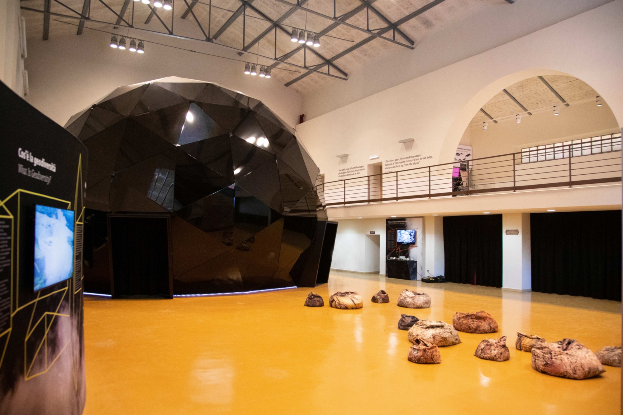 Interno del Museo MUBIA con grande installazione scura al centro della sala, pannelli espositivi e reperti geologici sul pavimento.