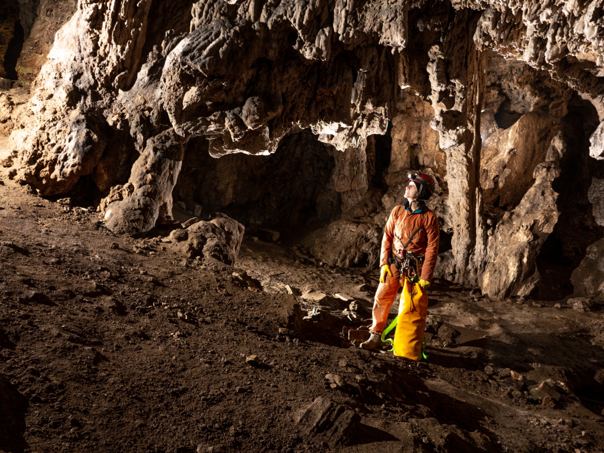 Speleologo con casco e tuta arancione all’interno di una grotta rocciosa.