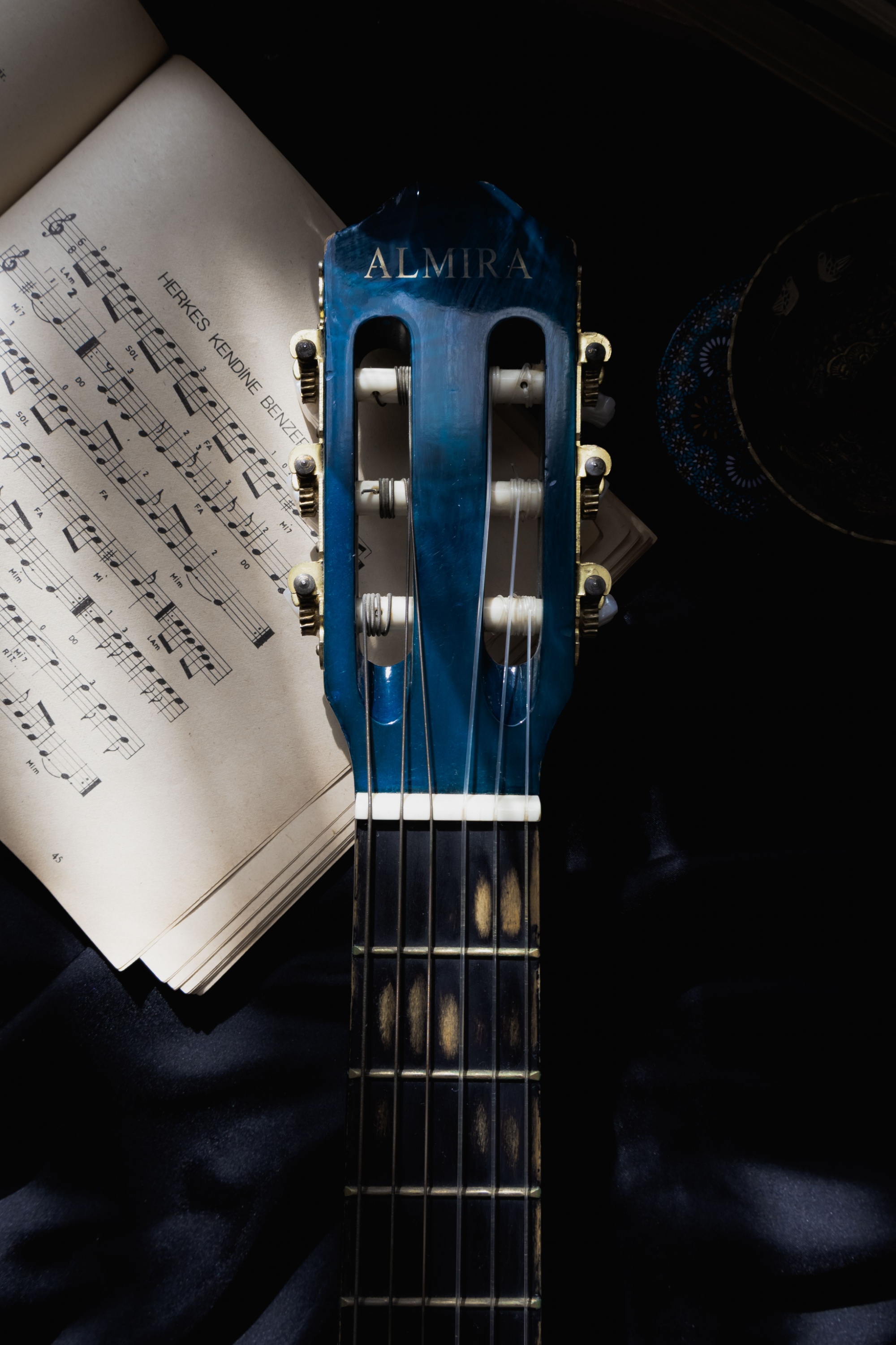 Immagine del manico di una chitarra blu con uno spartito musicale appoggiato sotto