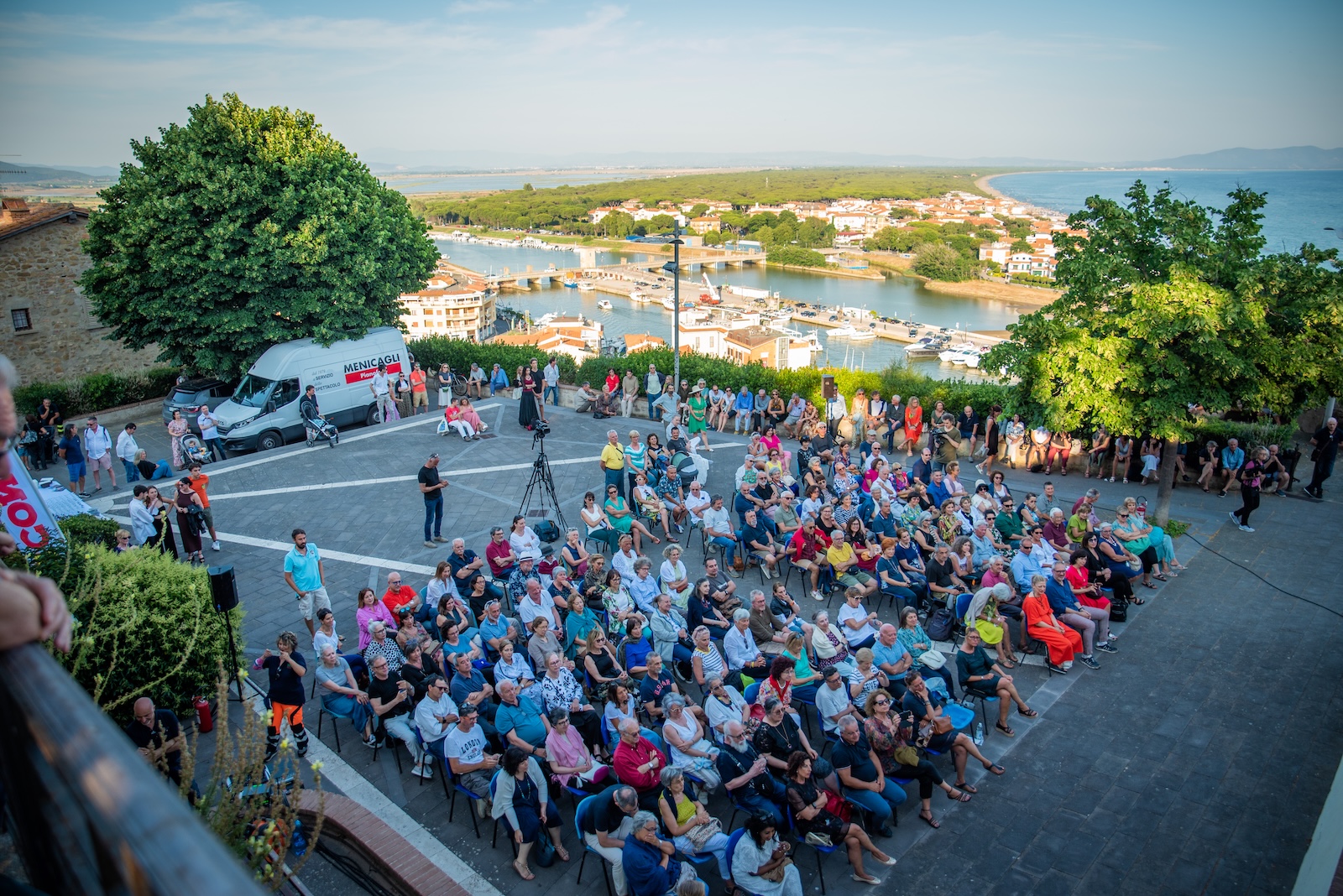 Immagine della piazza durante il concerto, con il mare sullo sfondo e molte persone sedute ad ascoltare
