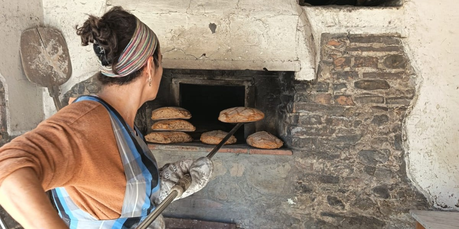 Donna al lavoro davanti al forno a legna del Mulino Parrini, mentre estrae con una lunga pala alcuni pani appena cotti