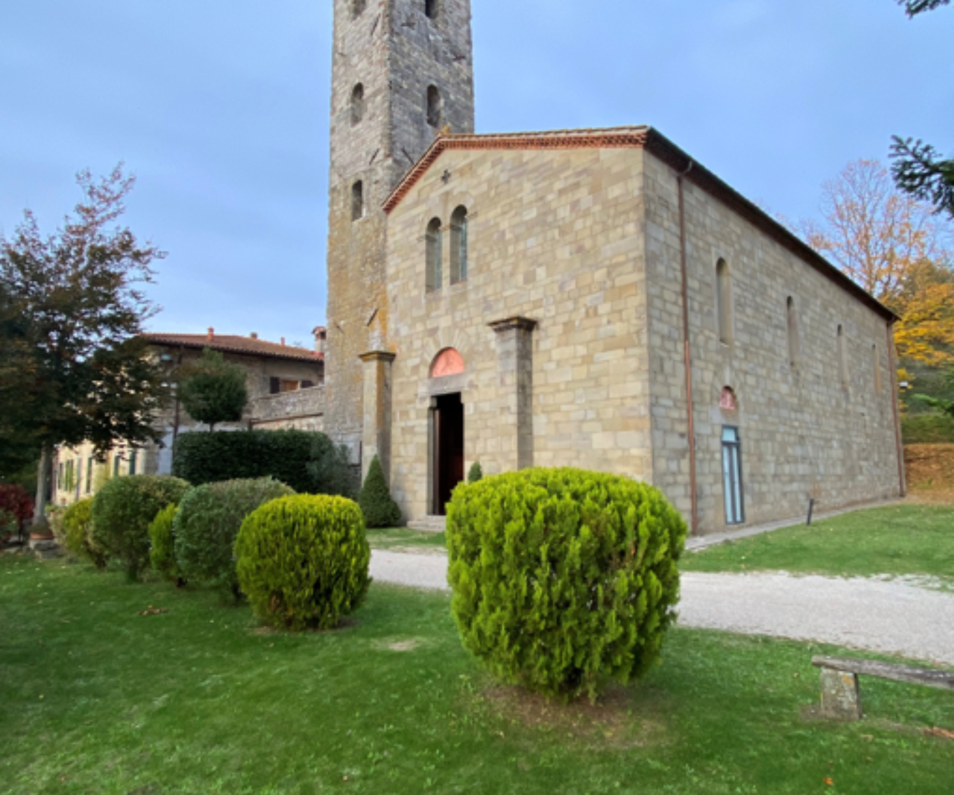 La facciata in pietra e la torre campanaria della Chiesa romanica di San Cresci in Valcava, circondata da un prato verde curato con cespugli tondeggianti