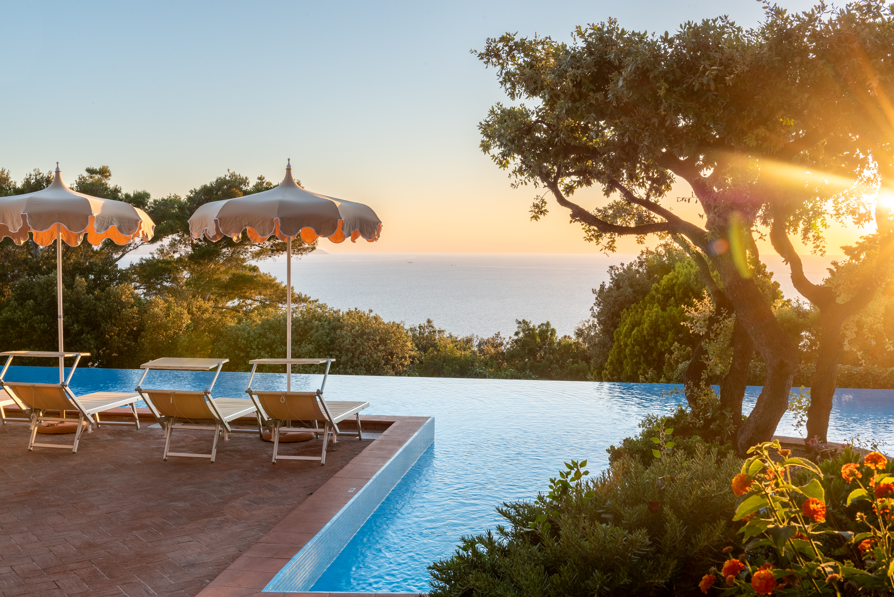 Piscina a sfioro con vista mare e tramonto, ombrelloni e lettini, isola d'Elba