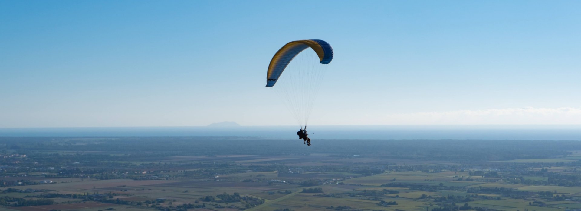 parapendio in volo sulla campagna col mare all'orizzonte