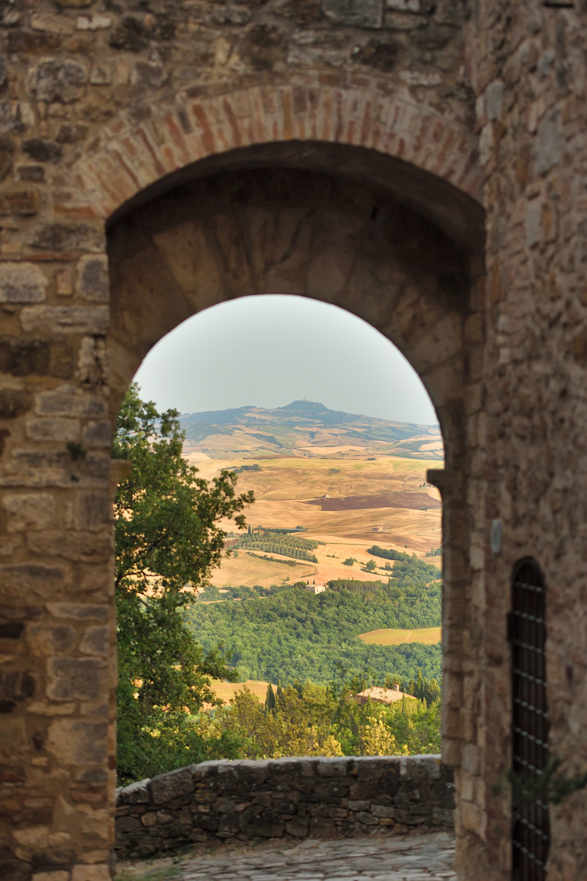 Arco in pietra del borgo di Vignoni con vista sul paesaggio della Val d’Orcia.