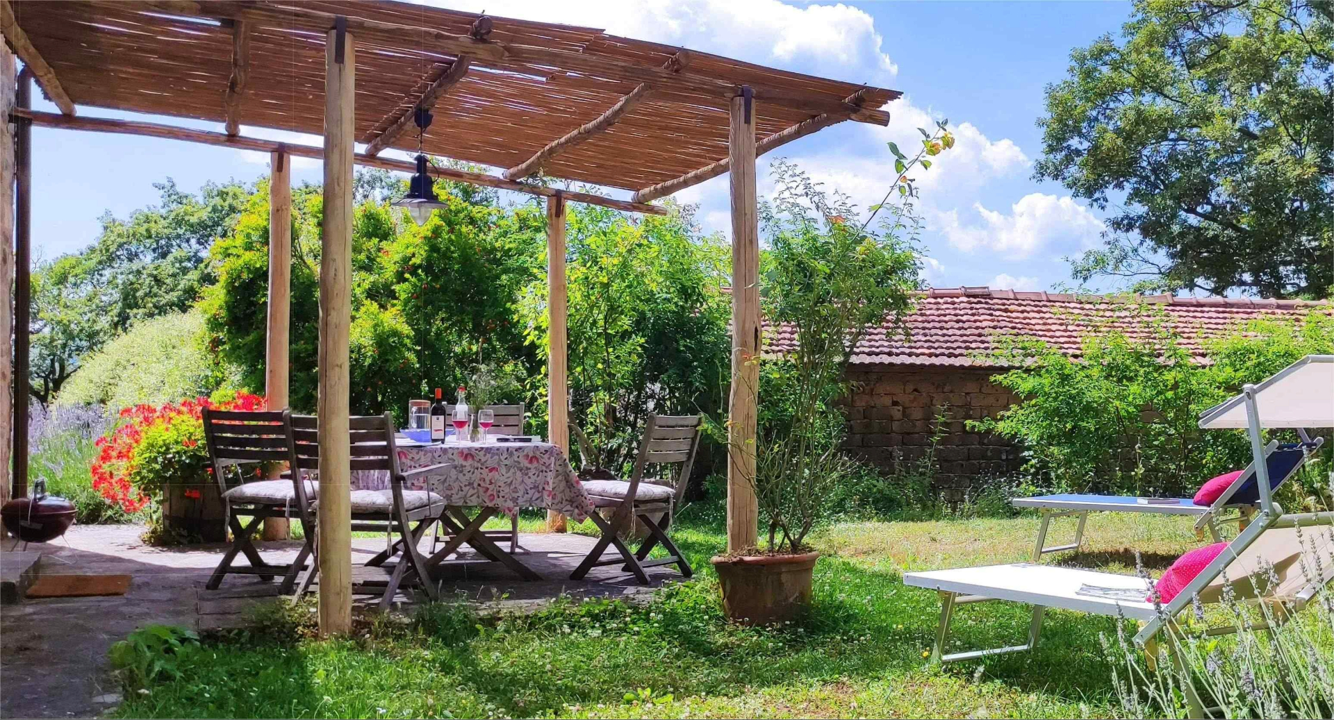 Area pranzo all'aperto con pergolato in legno e lettini in giardino