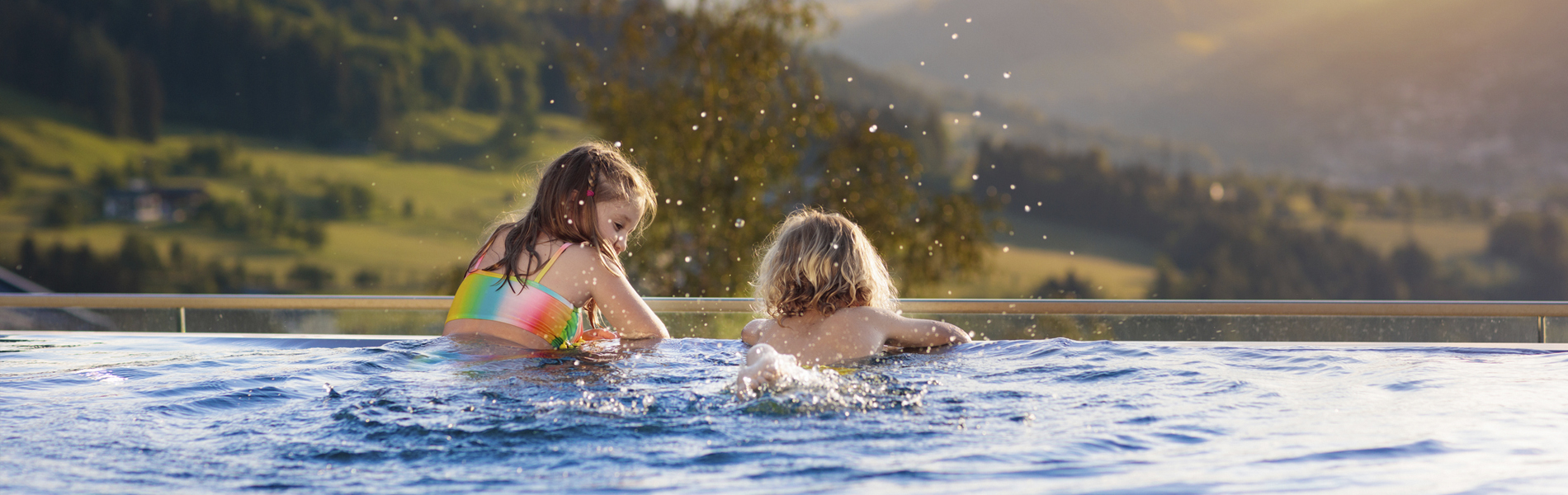 Two children having fun in an infinity pool overlooking a hilly landscape at sunset