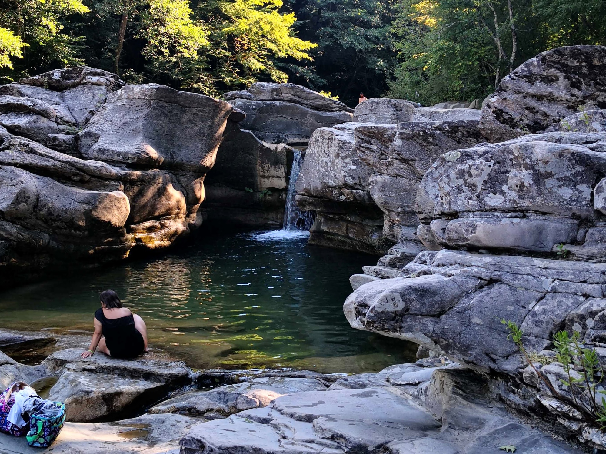 Acqua smeraldo, una cascatella e vegetazione lungo il Fiume Farma durante una giornata estiva con qualche bagnante.