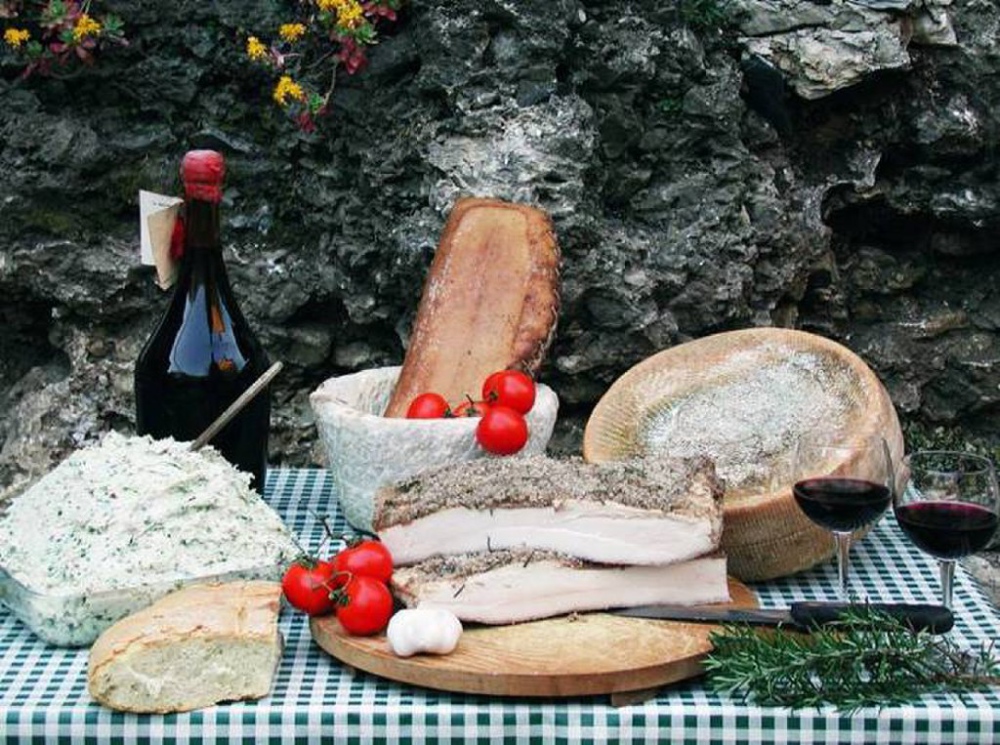 Prodotti tipici della Lunigiana Tavola imbandita con formaggio, pane, lardo di Colonnata e bicchieri di vino rosso